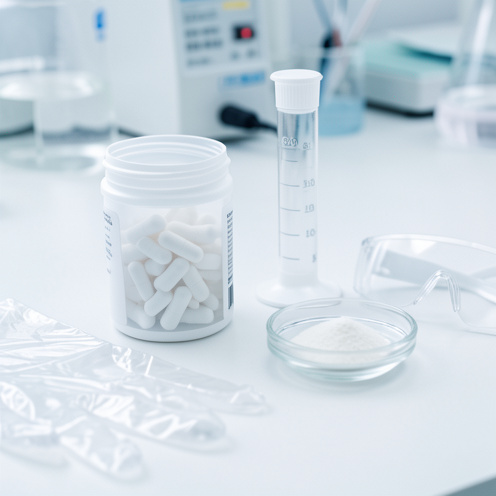 Présentation sobre d’un médicament avec des capsules, un flacon doseur et des accessoires de protection dans un environnement de laboratoire.